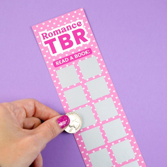 Pink 'Romance TBR' scratch-off bookmark with heart patterns on a purple background