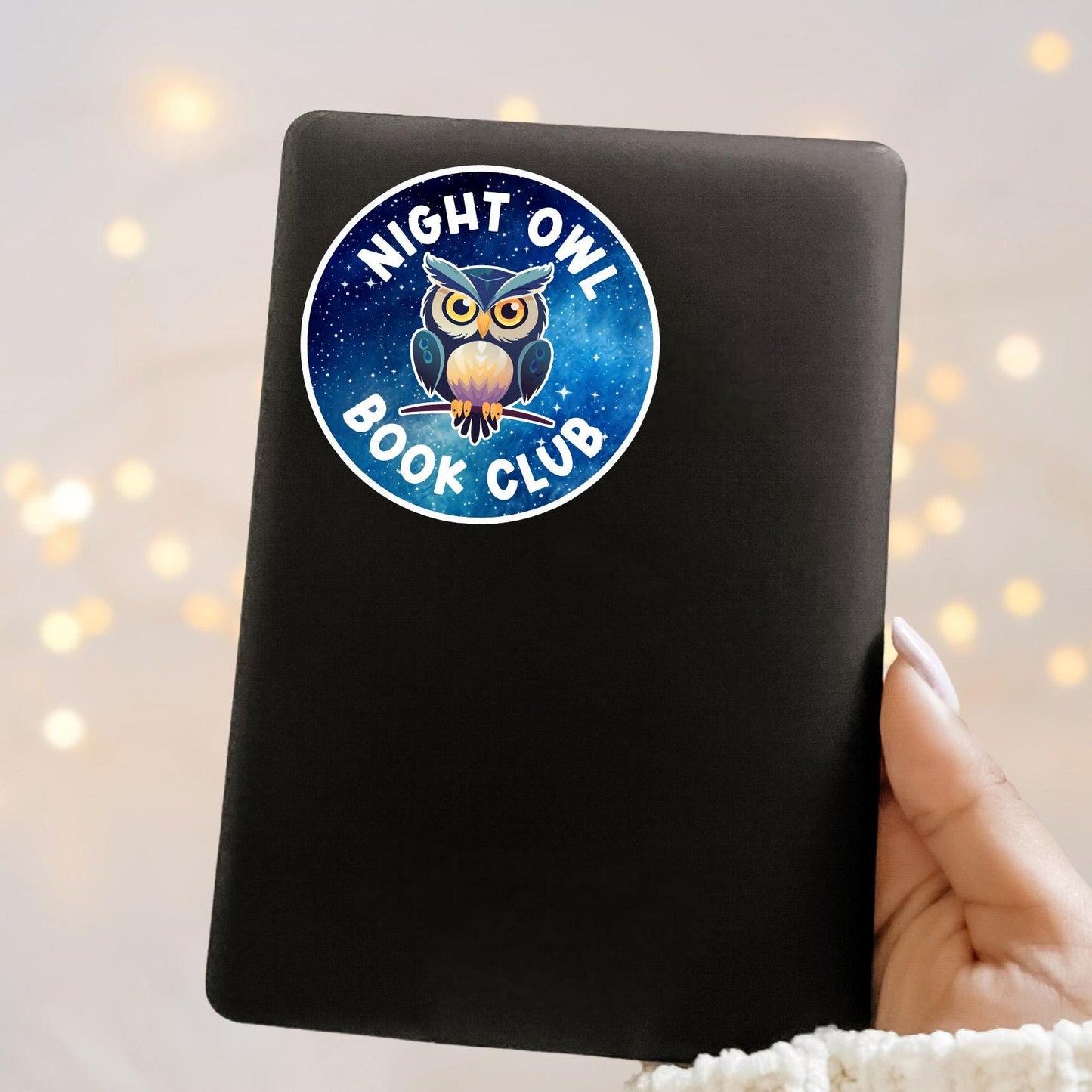 Black notebook with a 'Night Owl Book Club' sticker held against a soft, blurred background.