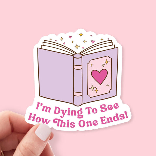 Sticker of an open book with a heart and "I'm Dying to See How This One Ends" text on a pink background