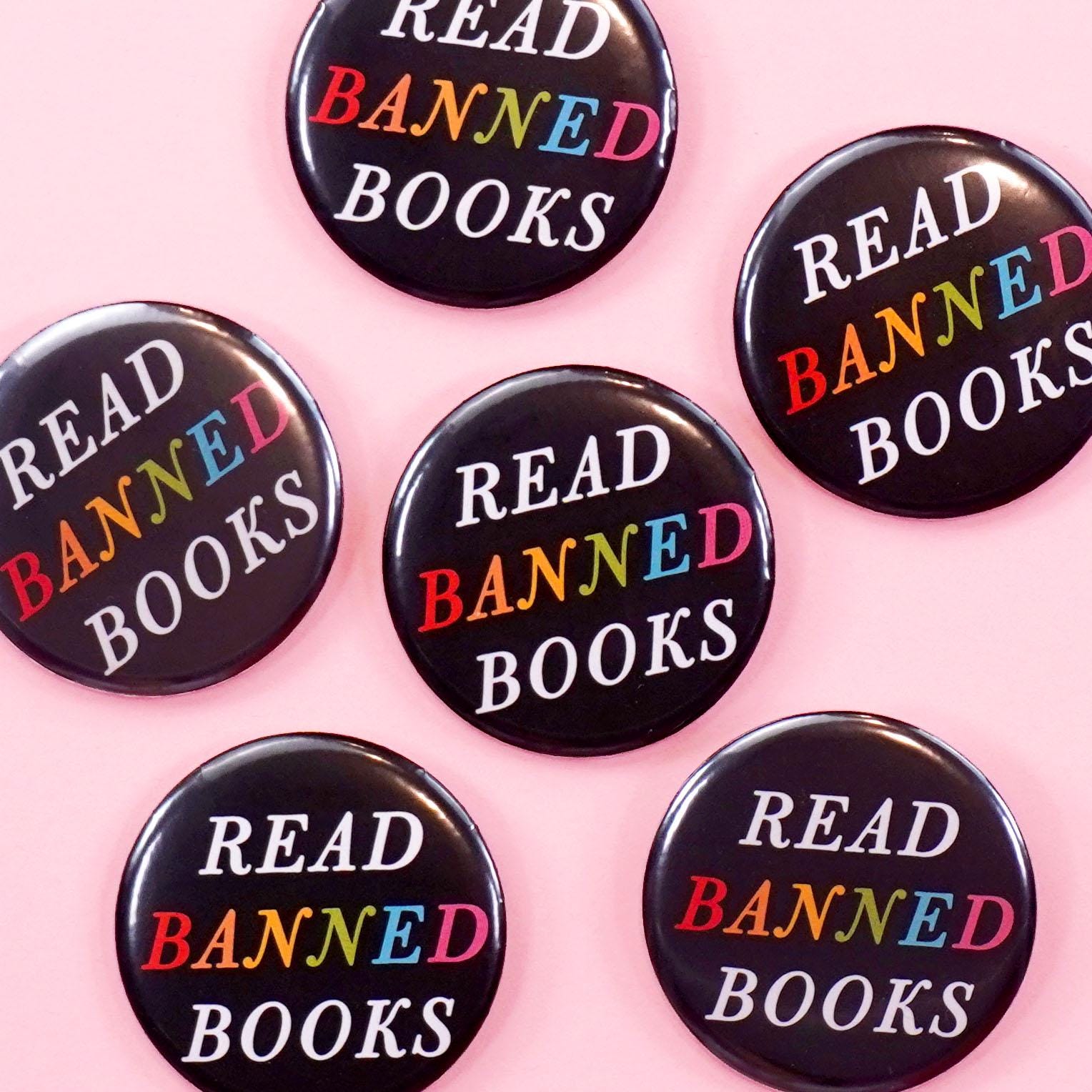 Black buttons with rainbow colored 'Read Banned Books' text on a pink background