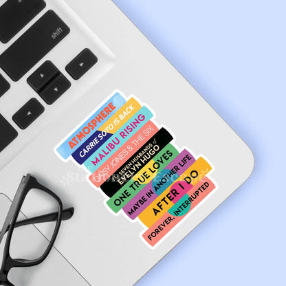 Colorful Taylor Jenkins Reid book title stickers on a laptop keyboard with glasses and a blue background